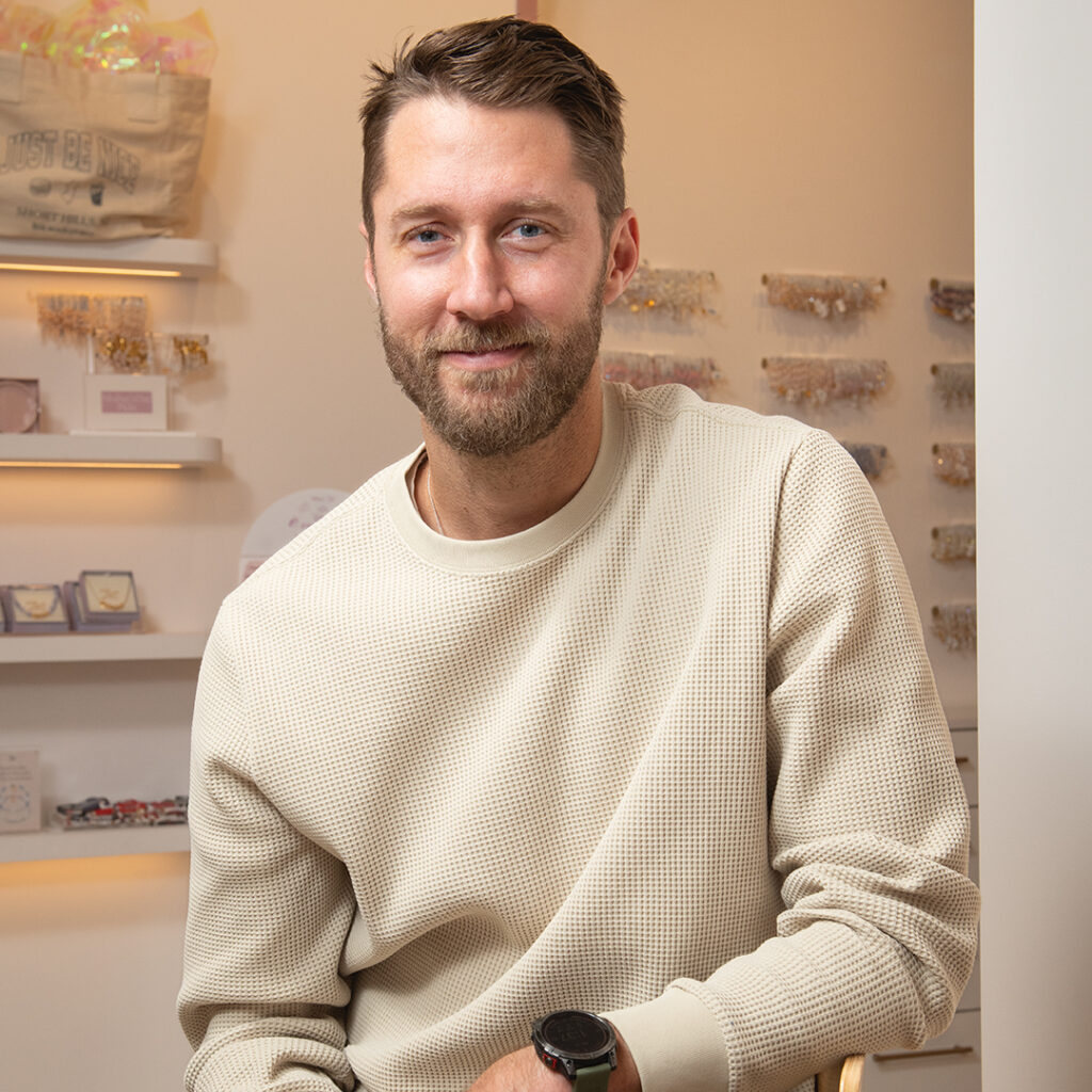 CEO Bill Carrig sits in store with Little Words bracelets hanging on wall behind him.