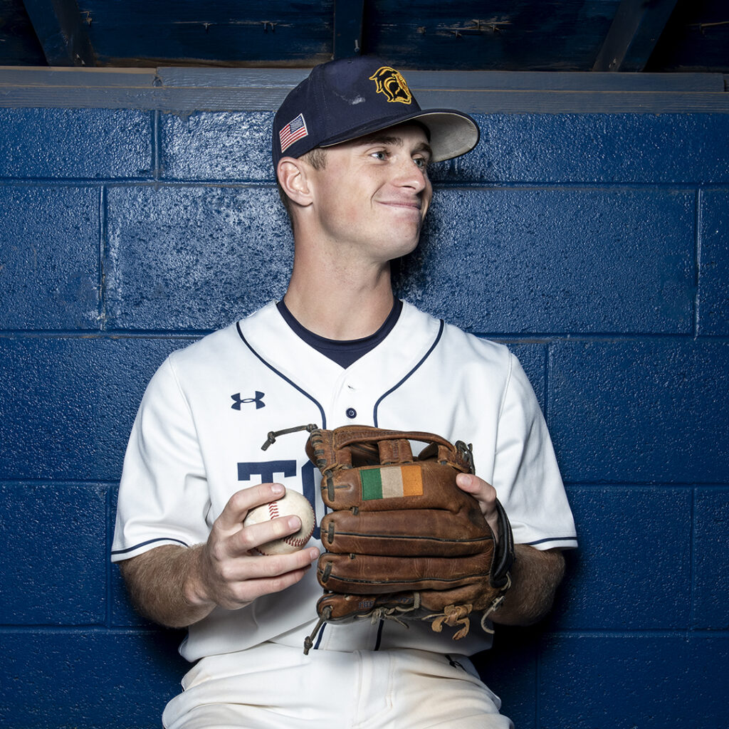 Baseball player sits in the dugout holding a glove.