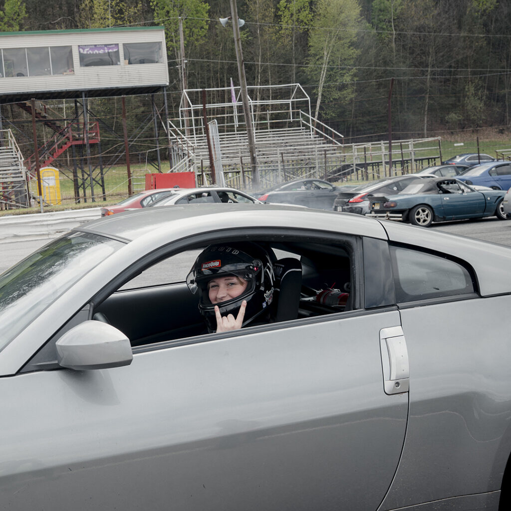 Female motersport drifter sits in car with helmet on, ready to race.