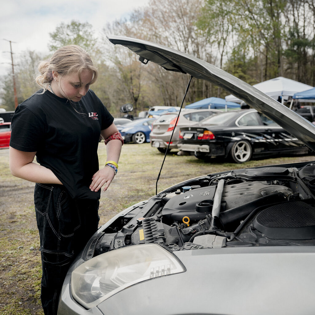 Female drift car racer checks oil between races.