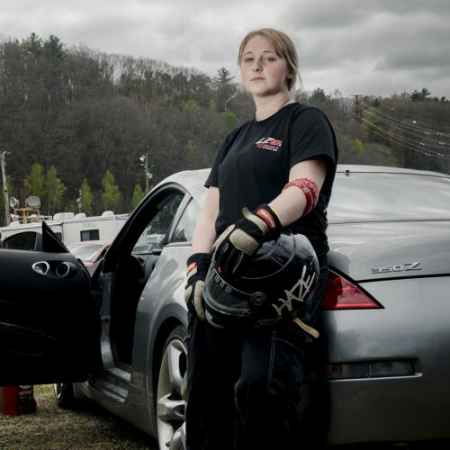 Female motorsport participant stands against her drift car at Evergreen Raceway in Pennsylvania.