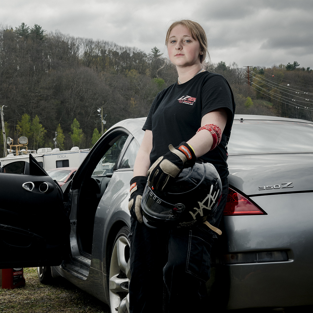 Female motorsport participant stands against her drift car at Evergreen Raceway in Pennsylvania.